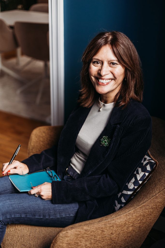 Katya Corbineau Bergue, souriante, assise dans son cabinet avec un carnet et un stylo.